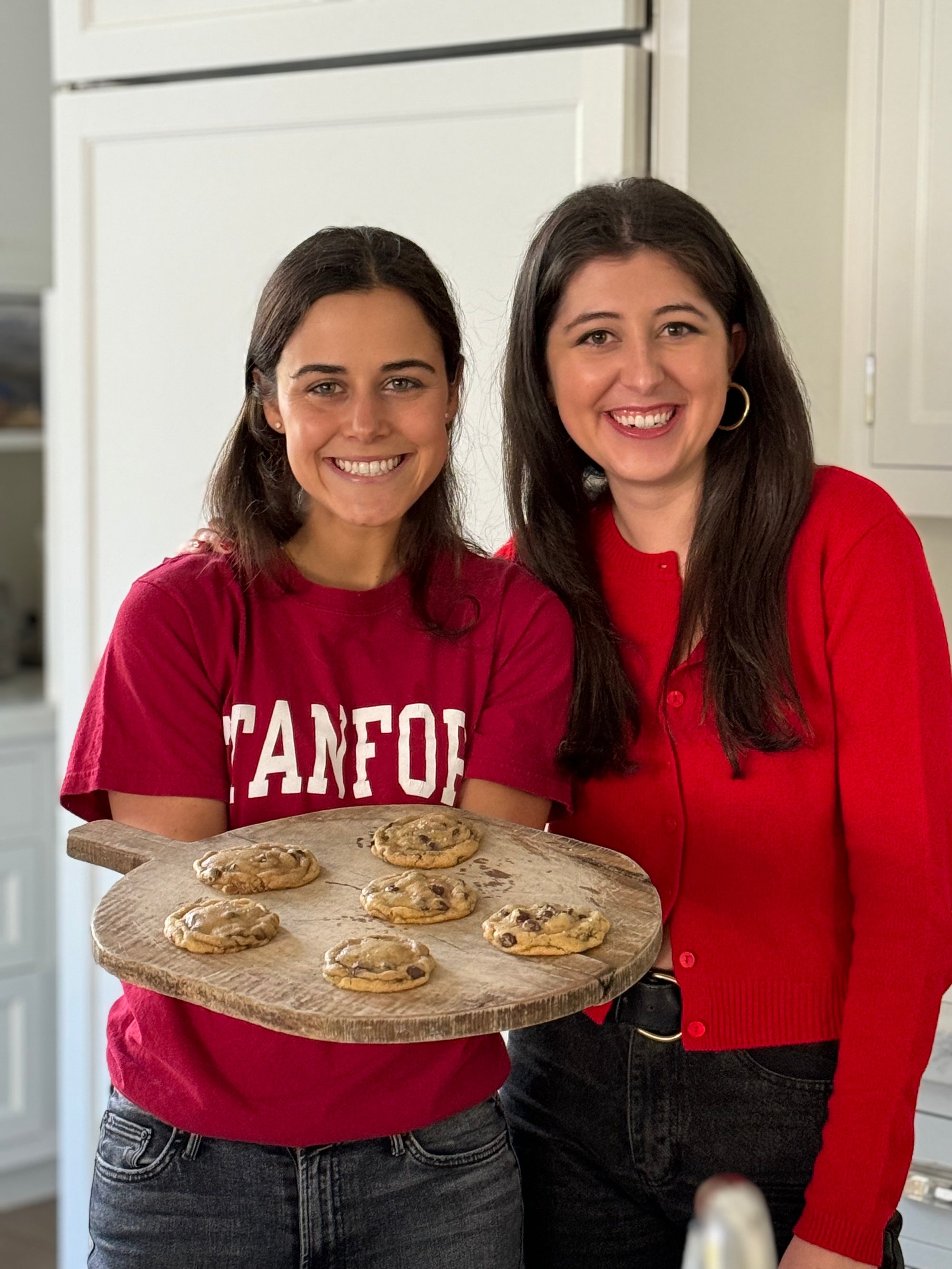 Two women in a kitchen holding a tray of cookies
