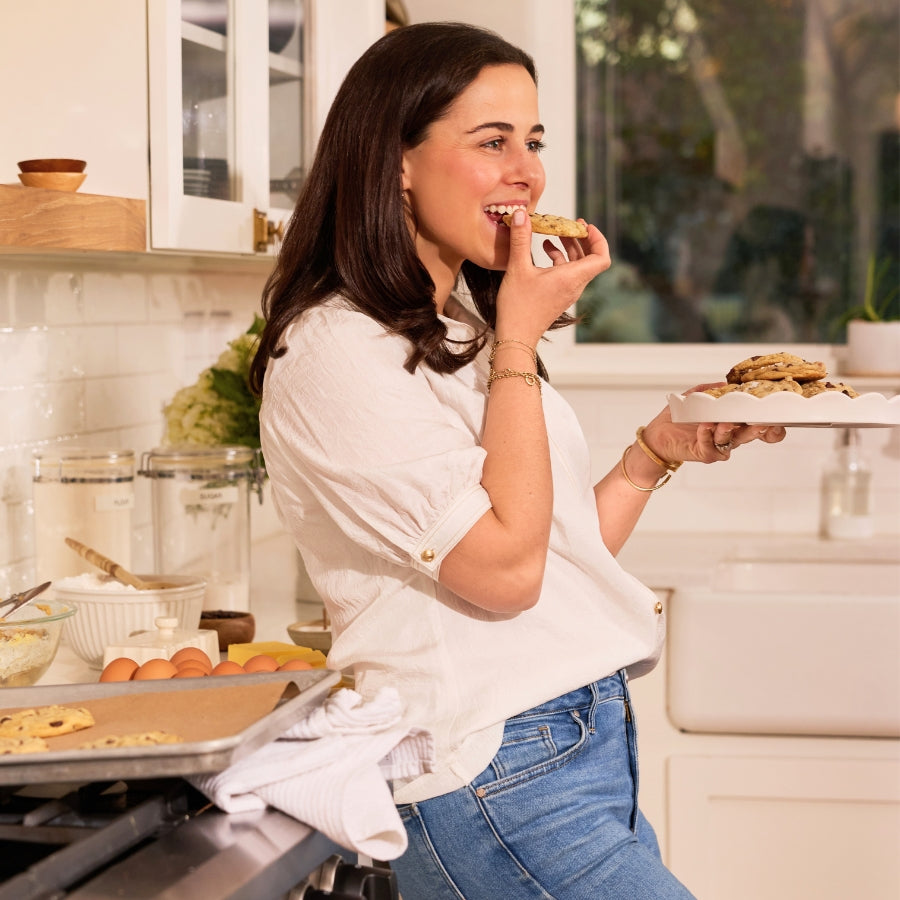 Marge eating a cookie in a kitchen with baking trays and ingredients.